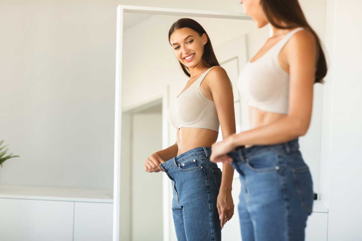 Frau schaut in Spiegel mit viel zu grosser Hose